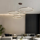 Circular LED pendant light with gold finish, hanging above a modern living room featuring a couch, table, houseplant, and wooden flooring.