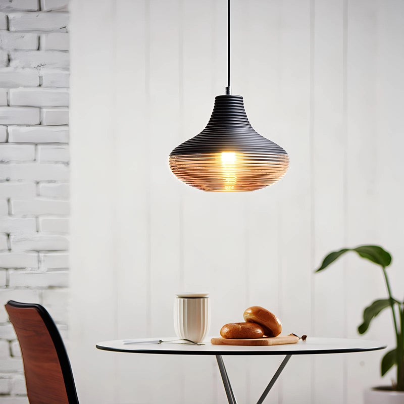 Designer Ribbed Glass Pendant Light with modern industrial design hanging above a wooden table and chairs, illuminating the kitchen space with a warm orange glow.