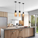Designer ribbed glass pendant light hanging above a modern industrial kitchen with wooden cabinetry, grey countertops, and potted plants.