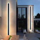 Minimalist LED wall sconce in a sleek vertical rectangular design, 48W, 8x120 cm, dimmable with motion detector, mounted on an exterior wall with modern decor and adjacent outdoor furniture.