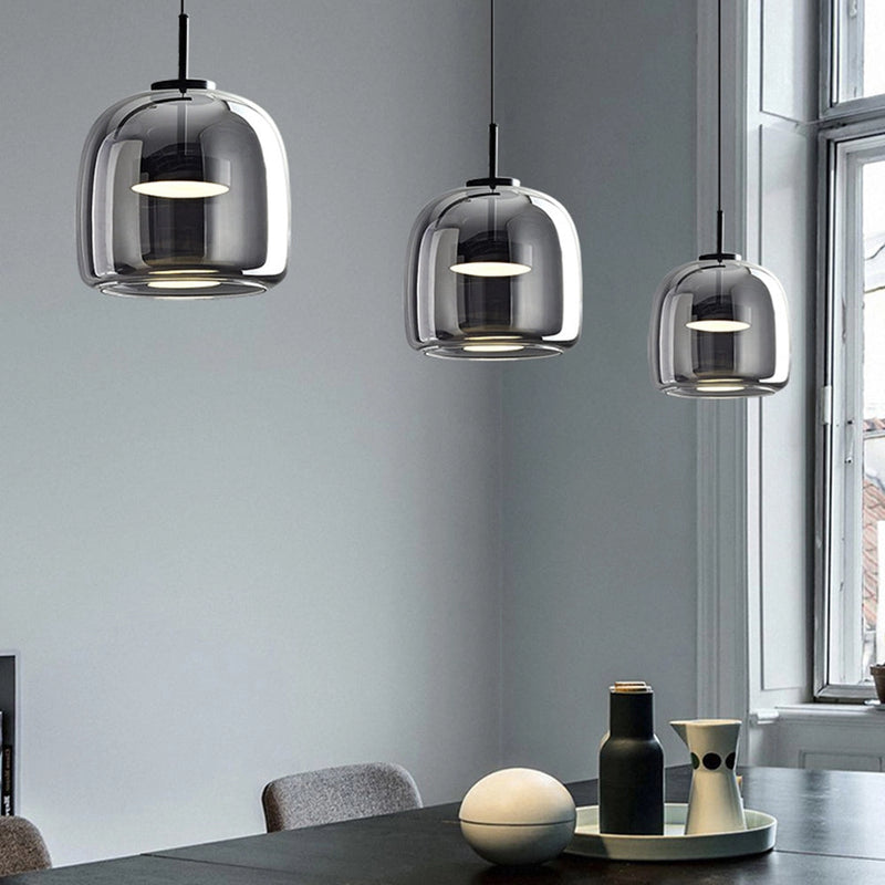 Modern glass pendant light with brass accents hanging from ceiling, providing elegant illumination to interior space with a white and yellow color scheme, featuring a wooden table below.