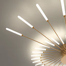 A black and gold starburst metal wall art sculpture with a mid-century modern design, displayed on a wall with a plant nearby.