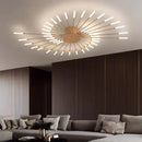 Modern starburst wall art in black and gold metal, dimmable, mounted on a wooden wall above a brown couch in a mid-century styled living room.