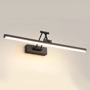 Sleek black dimmable LED picture light, cordless and adjustable, wall-mounted above a wooden frame in a still life setting.