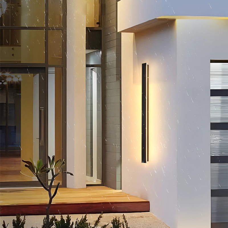 Slim vertical LED wall sconce in a minimalist design, 120CM dimmable, mounted on a wooden wall inside a modern, stylish interior with plants.