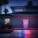 Slim Vertical LED Wall Sconce, 30CM RGB with motion sensors, mounted on an exterior wall next to a door, surrounded by a modern building facade, greenery, and blue sky background.