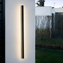 Slim Vertical LED Wall Sconce in White, 120CM, mounted on an exterior facade with sunlight casting through surrounding plants and trees.