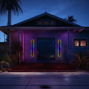 Slim Vertical LED Wall Sconce illuminating the exterior of a building near a garage door and window, with surrounding plants visible. The light is in RGB mode with motion sensors, casting a purple hue.