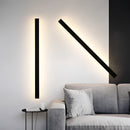 Slim Vertical LED Wall Sconce mounted on a grey wall above a wooden floor, next to a grey couch in a modern, minimalist interior design setting.